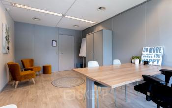Ruime kantoorruimte met houten vloer, vergadertafel en comfortabele stoelen, ideaal voor vergaderingen en werk. Voorzien van opbergruimte en decoratieve elementen op Overcingellaan 17, Assen, voor kantoorruimte huren.