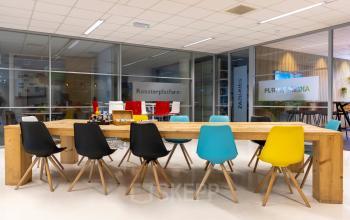 Vergaderruimte in een modern kantoorpand op de Amalialaan 126, Baarn. Verschillende gekleurde stoelen rondom een houten tafel. Glaswanden scheiden ruimtes.