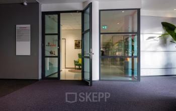 Entree van het kantoorpand op Amalialaan 126 in Baarn met glazen deuren en groene planten, ideaal voor kantoorruimte huren.