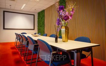 Vergaderruimte in kantoorpand op Amalialaan 126, Baarn met moderne tafel, blauwe stoelen en decoratieve bloemen. Ideaal voor kantoorruimte huren.