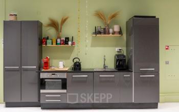 Gemeubileerde pantry van een kantoorpand met moderne grijze kastjes, een koffiezetapparaat en decoratieve elementen. Ideaal voor wie kantoorruimte wilt huren in Baarn.