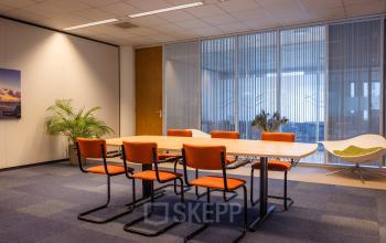 Kantoorruimte huren op Amalialaan 126 in Baarn met een vergadertafel en oranje stoelen, omringd door rustige decoraties en een glazen wand.