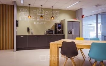 Moderne pantry in kantoorpand met een houten tafel, kleurrijke stoelen en keukenapparatuur op Amalialaan 126, Baarn.