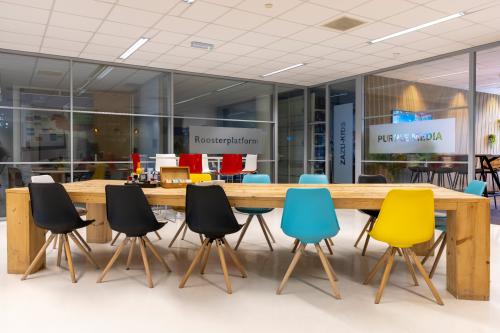 Vergaderruimte in een modern kantoorpand op de Amalialaan 126, Baarn. Verschillende gekleurde stoelen rondom een houten tafel. Glaswanden scheiden ruimtes.