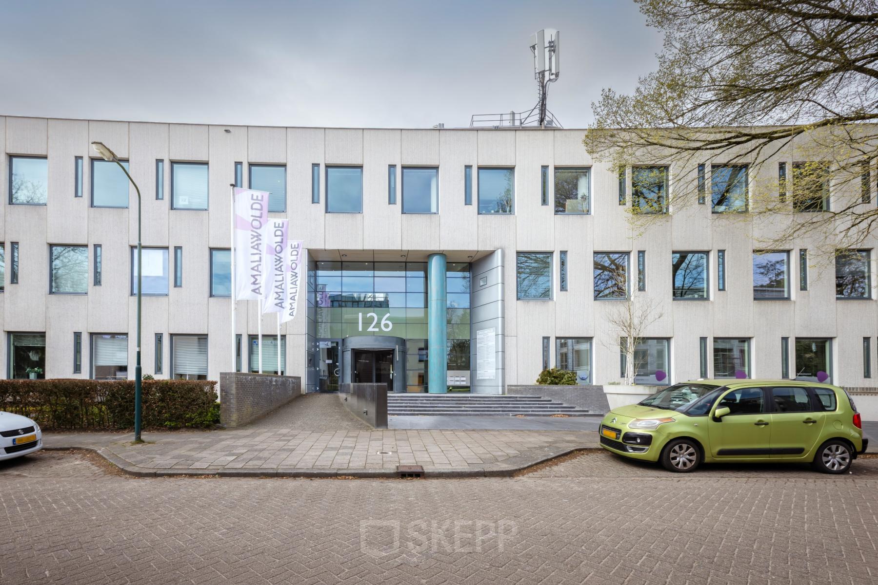 Vooraanzicht van kantoorpand op Amalialaan 126 in Baarn; modern gebouw met strakke gevel en parkeerplaats. Ideaal voor kantoorruimte huren.