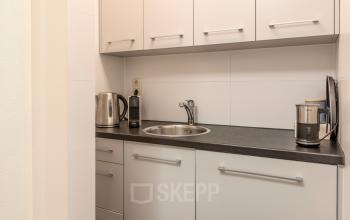 Functionele pantry in een Barendrechts kantoorpand met witte kasten en een donker aanrechtblad, ideaal voor een snelle break tijdens het kantoorwerk.