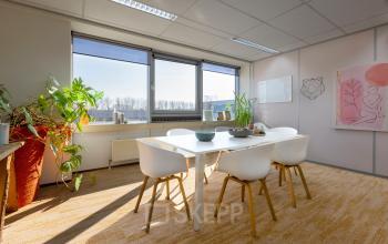 Lichte kantoorruimte op Kamerlingh Onnesweg 10, Barendrecht, met een witte tafel en stoelen, omringd door ramen en planten.