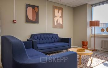 Stijlvolle lounge in kantoorpand aan de Kamerlingh Onnesweg 10, Barendrecht, met donkerblauwe banken, kunst aan de muur en houten salontafel. Kantoorruimte huren in een uitnodigende omgeving.