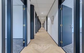 Strak ingerichte gang met openstaande deuren in een modern kantoorgebouw aan de Rijtuigweg 10, ideaal om kantoorruimte te huren in Bergen op Zoom.