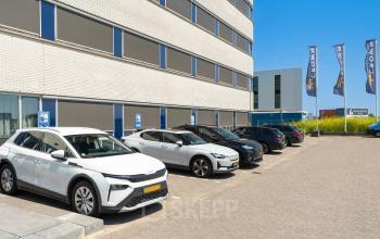 Parkeerplaats bij kantoorpand Tolnasingel 1-3 in Bodegraven met meerdere geparkeerde auto's naast een modern gebouw.