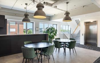 Gedeelde kantoorruimte met ronde tafels en stoelen, naast een lift en grote ramen met uitzicht op Tolnasingel 1-3 in Bodegraven. Ideaal voor kantoorruimte huren met modern interieur.