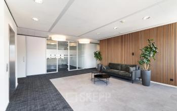 Moderne kantoorruimte op Tolnasingel 1 - 3 in Bodegraven, met glazen wanden, houten wandbekleding en een stijlvolle bank. Ideaal voor wie een kantoorpand wil huren.