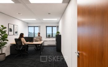 Lichte kantoorruimte op Tolnasingel 1 - 3, Bodegraven, met twee personen bezig aan een bureau. Moderne inrichting met planten en minimalistische kunstwerken aan de muur.