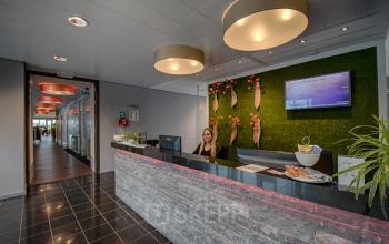 Kantoorpand aan Tolnasingel 1-3, Bodegraven, met een moderne receptie en een medewerker achter de balie. Fraai verlichte ruimte met decoratieve groene muur.
