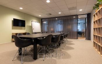 Moderne conferentieruimte met een lange zwarte tafel en stoelen, tegen een achtergrond van glazen wanden in een kantoorpand voor huur in Bodegraven.