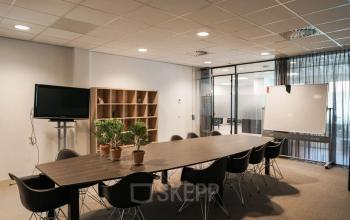 Vergaderruimte in kantoorpand aan de Marktstraat 1-7, Bodegraven, met lange tafel, stoelen, televisiescherm en whiteboard. Ideaal om kantoorruimte te huren voor zakelijke bijeenkomsten.