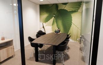 Moderne vergaderruimte in kantoorpand op Marktstraat 1-7, Bodegraven, met een grote houten tafel en zes zwarte stoelen, omringd door een groene fotomuur.