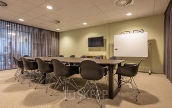 Moderne vergaderruimte in Bodegraven met grote tafel omringd door strakke stoelen en een whiteboard, ideaal voor kantoorruimte huren bij Marktstraat 1-7.