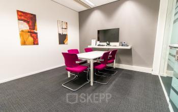 Vergaderruimte in modern kantoorpand, Ceresstraat 1 in Breda Centrum-Station, met een tafel, roze stoelen en kunst aan de muur. Ideaal voor kantoorruimte huren.