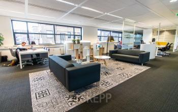 Moderne kantoorruimte in Breda Centrum-Station, met veel daglicht en comfortabele zithoeken. Werknemers zijn bezig met administratieve taken. Ideaal om een kantoorpand te huren.