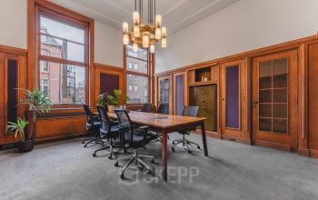 Kantoorruimte huren in Breda Centrum-Station op Ceresstraat 13 met een klassieke vergaderruimte, houten lambrisering, grote ramen en een lange tafel met stoelen.