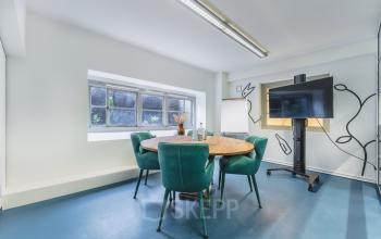 Moderne en lichte kantoorruimte met ronde tafel, comfortabele stoelen en een groot scherm, ideaal voor vergaderingen. Beschikbaar voor huur op Ceresstraat 13 in Breda Centrum-Station.