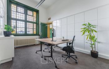 Lichte kantoorruimte te huur op Ceresstraat 13 in Breda Centrum-Station met grote ramen, een houten bureau en bureaustoelen, omgeven door groene planten.