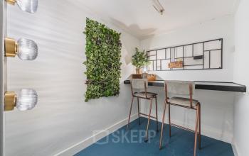 Kantoorruimte te huur op Ceresstraat 13, Breda Centrum-Station. Compacte ruimte met groene wanddecoratie en twee hoge stoelen aan een smalle tafel, ideale setting voor rustig werken.