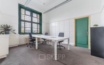 Kantoorruimte te huur op Ceresstraat 13 in Breda Centrum-Station met drie bureaustoelen, witte tafels en een groen geverfde deur. Grote ramen met glas-in-lood en enkele planten aanwezig.