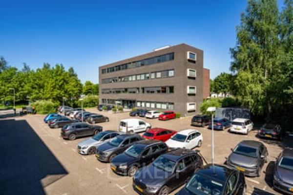 Kantoorpand in Breda Noord-West, Westboek 36-66, met parkeerplaats vol auto's, omgeven door groene bomen, onder een heldere blauwe lucht. Geschikt voor bedrijven die kantoorruimte willen huren.