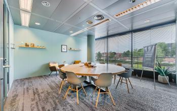 Kantoor op Heerbaan 14, Breda met moderne vergaderruimte. Grote houten tafel met gestoffeerde stoelen, ramen bieden veel natuurlijk licht. Ideaal voor kantoorruimte huren.