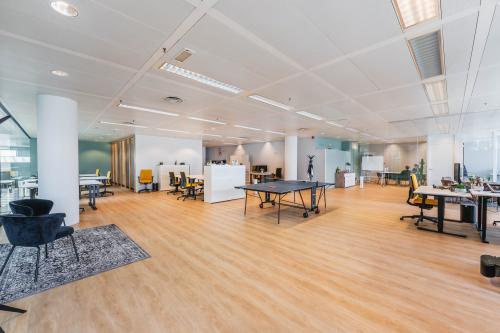 Lichte, ruime kantoorruimte huren aan de Heerbaan 14, Breda. Open indeling met bureaus, vergadertafel, en tafeltennistafel. Moderne details en planten creëren een uitnodigende werkomgeving.