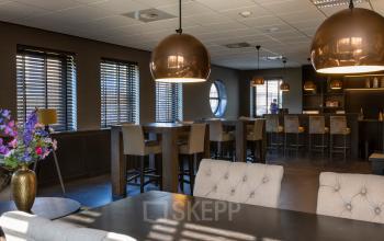 Moderne kantoorruimte huren in kantoorpand aan Takkebijster 57A, Breda Oost-Brabantpark. Gemeubileerd interieur met hoge tafels, barkrukken en ronde lampen, perfect voor een open werkomgeving.