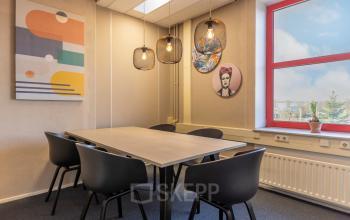 Stijlvolle kantoorruimte huren in Breda Oost-Brabantpark met moderne kunst aan de muur, grote tafel en stoelen onder sfeervolle lichten.