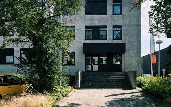 Entree van kantoorpand aan de Druivenstraat 25-31 in Breda Oost, met bomen en een geparkeerde auto voor de ingang.