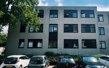 Moderne kantoorpand aan Druivenstraat 25-31 in Breda Oost met meerdere parkeerplaatsen aan de voorzijde onder een blauwe hemel.