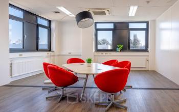 Vergaderruimte in kantoorpand Druivenstraat 25-31, Breda Oost, met rode stoelen rond een ovale tafel. Veel lichtinval door grote ramen. Geschikt voor kantoorruimte huren.