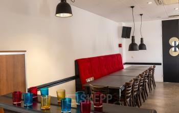 Herkenbare kantoorpand ambiance in Breda Oost aan Druivenstraat 25-31 met een strak ingerichte ruimte voorzien van een lange tafel en kleurrijke glazen op een kast.