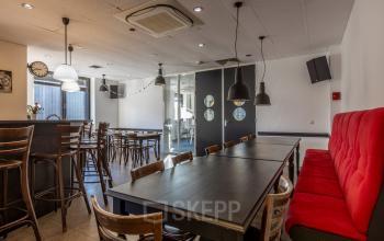 Een moderne kantoorruimte op Druivenstraat 25-31 in Breda Oost met houten tafels en stoelen, rode bank en decoratieve lampen. Geschikt voor huur, het kantoorpand biedt een veelzijdige omgeving voor werk.