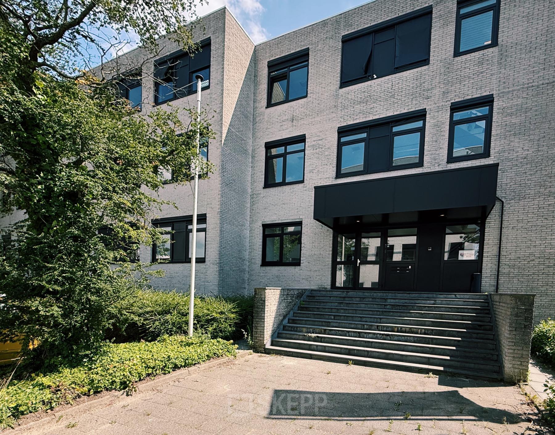 Het kantoorpand aan de Druivenstraat 25-31 in Breda Oost, geschikt voor kantoorruimte huren. De moderne gevel met grote ramen is omgeven door groen en betegelde paden.