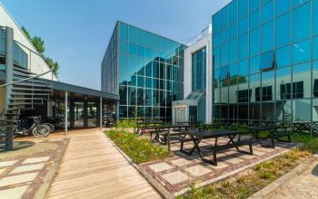 Moderne glazen gevel van een kantoorpand op Rietbaan 2-12 in Capelle aan den IJssel, omgeven door een strak aangelegd pad en fietsklemmen. Ideaal voor wie kantoorruimte wil huren.