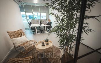 Kantoor in Capelle aan den IJssel met een modern interieur, tafels en stoelen, en planten. Twee personen voeren zakelijke activiteiten uit. Kantoorruimte huren mogelijk op Rietbaan 2-12.