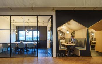 Moderne kantoorruimte in Capelle aan den IJssel met glazen wanden, vergaderruimte en individueel werkstation waar een persoon aan het werk is met een laptop.