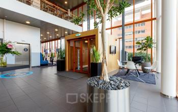 Entree van een modern kantoorpand in Capelle aan den IJssel met stijlvolle plantenbakken, een zithoek en een lift. Perfecte locatie voor kantoorruimte huren met comfortabele voorzieningen en een professionele uitstraling.