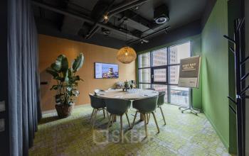 Vergaderkamer in kantoorpand op Rietbaan 40-42, Capelle aan den IJssel, met ronde tafel, zes stoelen, groene accentmuur en planten. Kantoorruimte huren met moderne en uitnodigende inrichting.