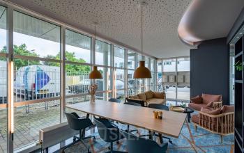 Moderne kantoorruimte huren in Capelle aan den IJssel met grote ramen, vergadertafel, stoelen en comfortabele zithoek, geschikt voor diverse zakelijke activiteiten.