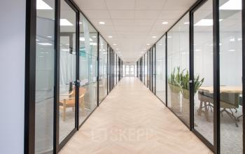 Heldere kantoorgang met glazen wanden en houten vloer in het kantoorpand aan Rivium Quadrant 75, ideaal voor wie kantoorruimte wil huren in Capelle aan den IJssel.