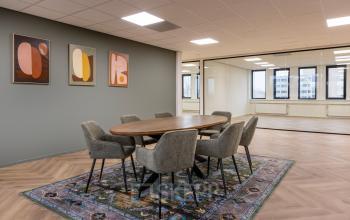 Moderne kantoorruimte met houten vergadertafel en zes stoelen op een kleurrijk tapijt, gelegen aan Vlierbaan 20, Capelle aan den IJssel. Ideale plek om kantoorruimte te huren voor zakelijke bijeenkomsten.