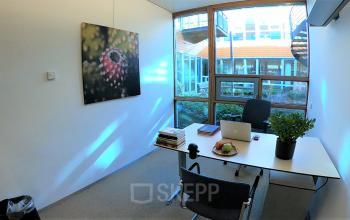 Licht kantoor op Multatulilaan 12 in Culemborg met grote ramen, een bureau met laptop, boeken en planten, ideaal voor kantoorruimte huren.