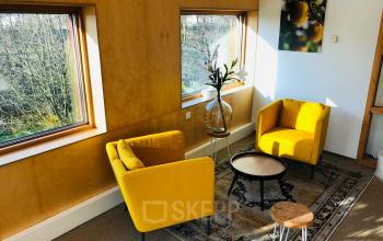 Gezellige kantoorruimte in Culemborg met gele stoelen, ronde tafels en grote ramen voor veel natuurlijk licht, ideaal voor informele vergaderingen.